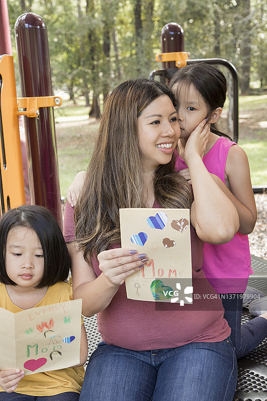 庆祝——母亲节——年轻的亚洲女孩和她们的妈妈在公园里。他们正在给她刚做的母亲节贺卡。图片素材