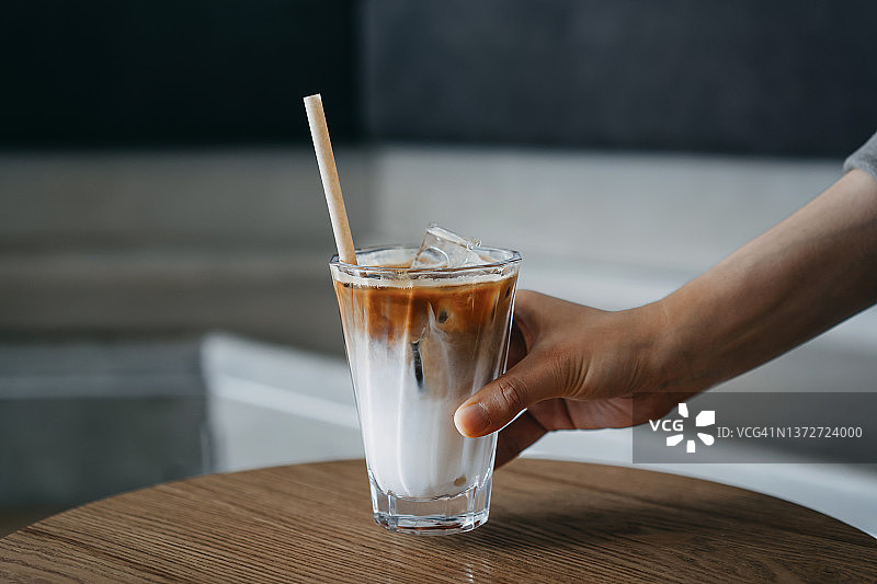 裁切的镜头，妇女的手拿着一杯冰咖啡与环保吸管服务在咖啡馆的木桌上图片素材