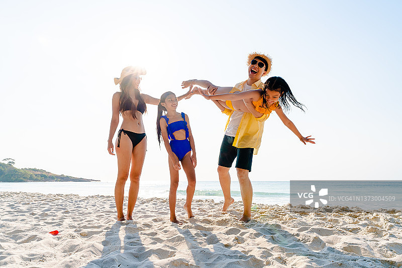 快乐的爸爸抱着会飞的女儿在沙滩上享受夏天的假期图片素材
