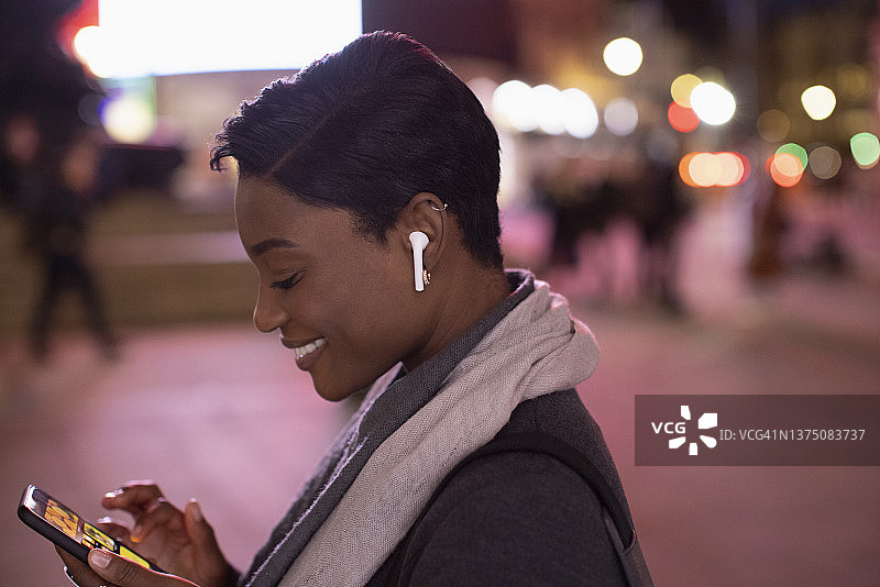 年轻女子戴着耳机在城市的夜晚使用智能手机图片素材