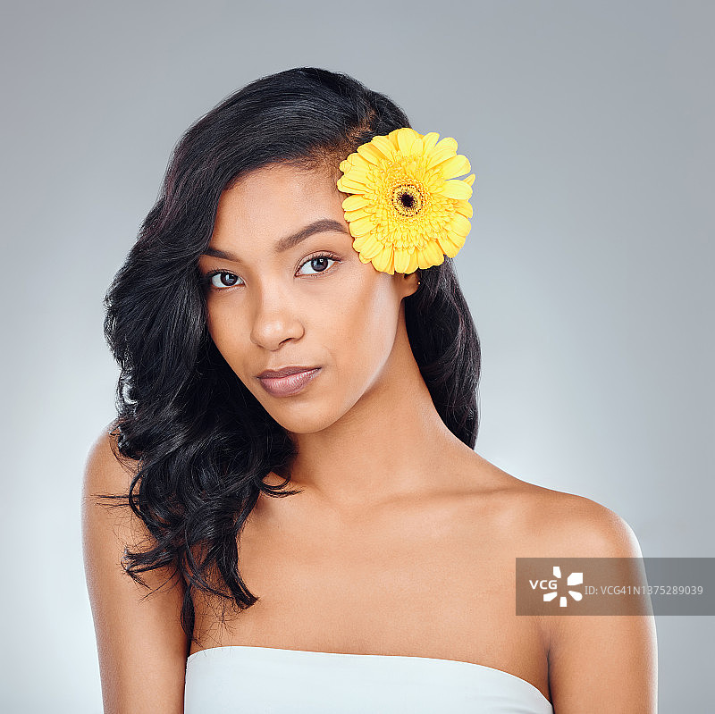 一个迷人的年轻女子的工作室肖像与黄色的花在她的头发在灰色的背景摆姿势图片素材