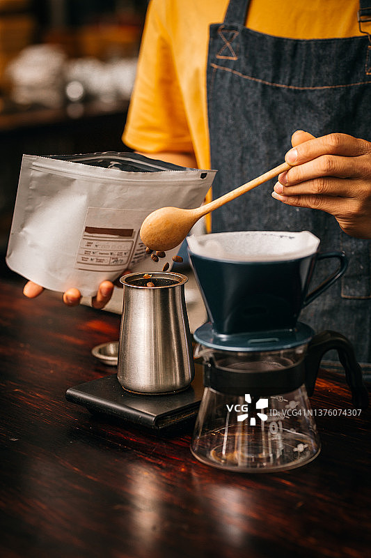年轻的亚洲男咖啡师，穿着黄色衬衫和蓝色围裙，用卡丽塔咖啡机煮咖啡图片素材