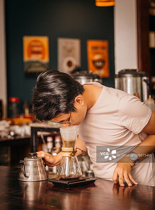 年轻的亚裔男咖啡师，穿着白衬衫，闻着用化学咖啡机煮咖啡的味道图片素材