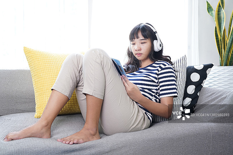 年轻女子躺在沙发上看书，听音乐放松图片素材