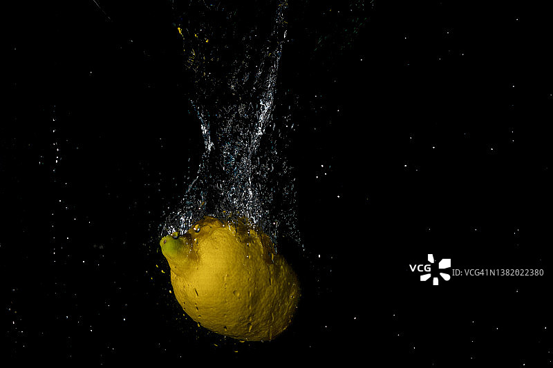 新鲜的黄色柠檬水泼在黑色背景图片素材