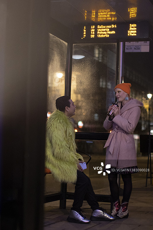 一对时髦的年轻夫妇晚上在城市公交车站聊天图片素材