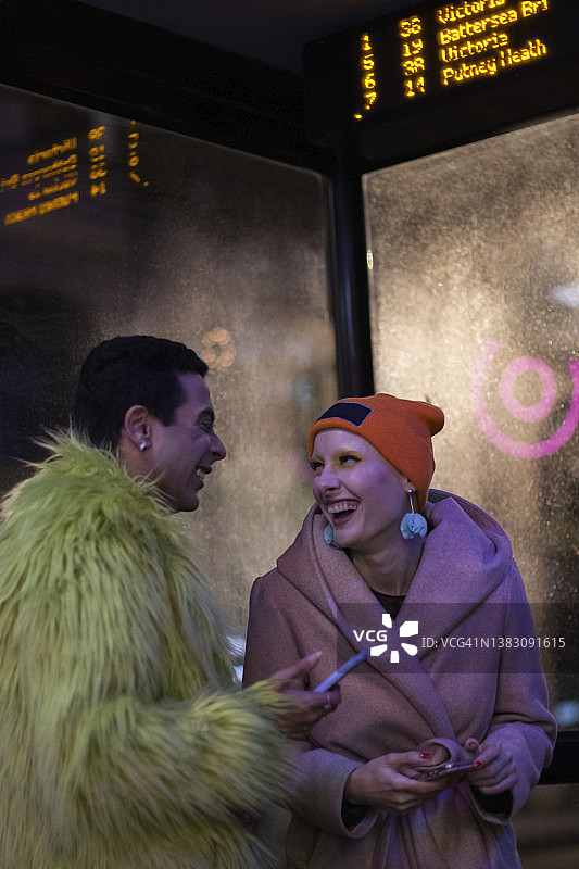 快乐时尚的夫妇在城市公交车站晚上智能手机图片素材