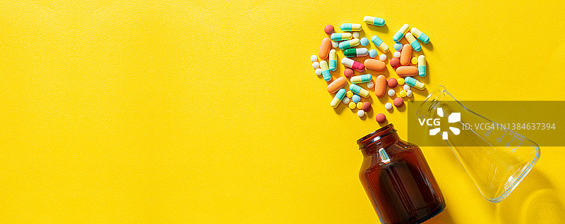 药丸和药丸瓶在黄色背景，彩色药片和药丸胶囊从玻璃瓶在黄色背景堆各种各样的药片和药丸。卫生保健特写副本图片素材