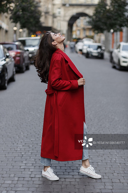 一个年轻的黑发女人穿着一件红色的外套，望着天空微笑着图片素材
