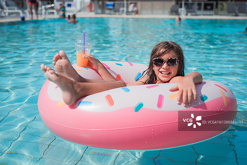 戴着太阳镜的女孩躺在一个甜甜圈形状的漂浮物在游泳池里图片素材