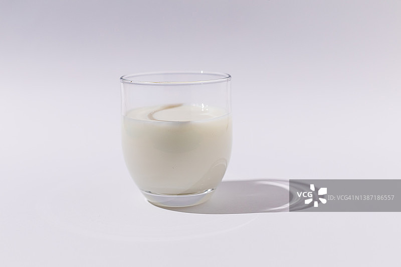 满杯牛奶在强光下白色背景。乳品、短缺、钙、生长、饮料理念图片素材