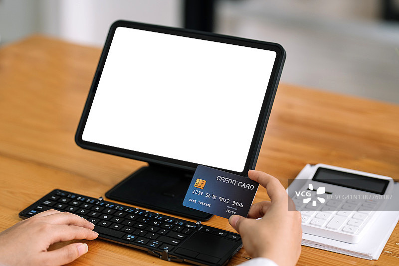 近距离的妇女手握信用卡和使用笔记本电脑，平板电脑空白的白色屏幕。网上购物的概念。图片素材