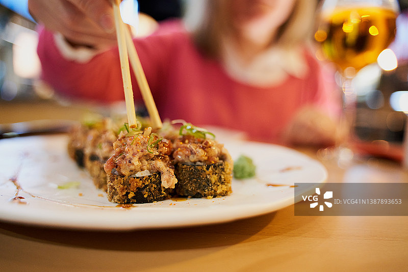 在一家日本餐馆，一个白人妇女用筷子从盘子里夹寿司。食品的概念图片素材