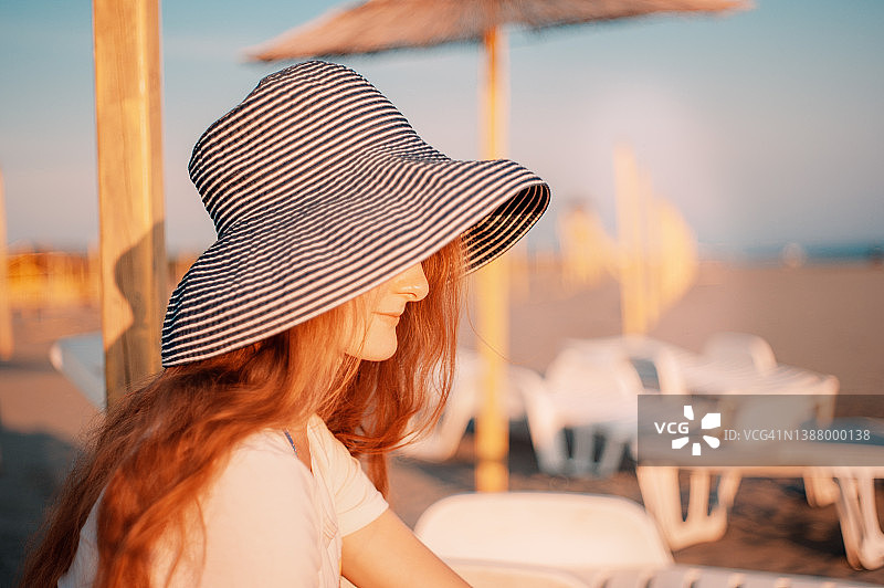 戴太阳帽的红发年轻女子的肖像再次出现在海滩上图片素材