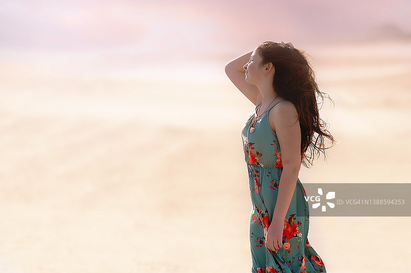 侧面的十几岁的女孩站在沙滩上，她长长的棕色头发吹在风中图片素材