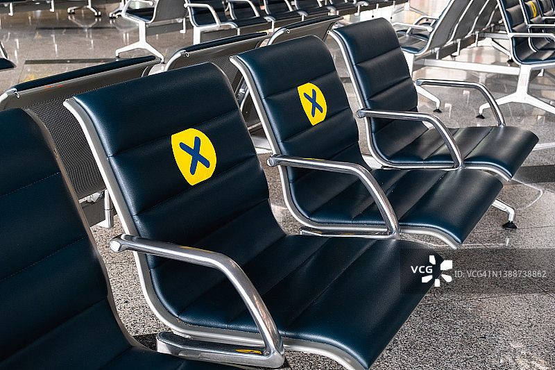 一张带有黄色标志的新贴纸贴在机场的一张椅子上，与其他乘客保持一个座位的距离。保持距离，保护和防范新冠肺炎、冠状病毒的传播风险。隔离和大流行期间的免费座位。图片素材