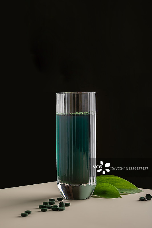 绿色排毒饮料与螺旋藻在一个杯子和药丸上的极简主义成分。维生素、健康、自我保健理念图片素材