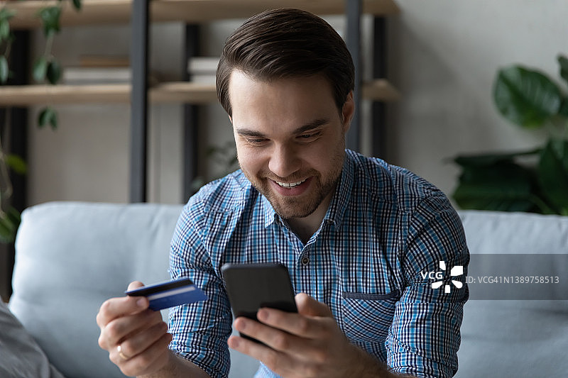 微笑的男子手持智能手机，用信用卡在线购物图片素材