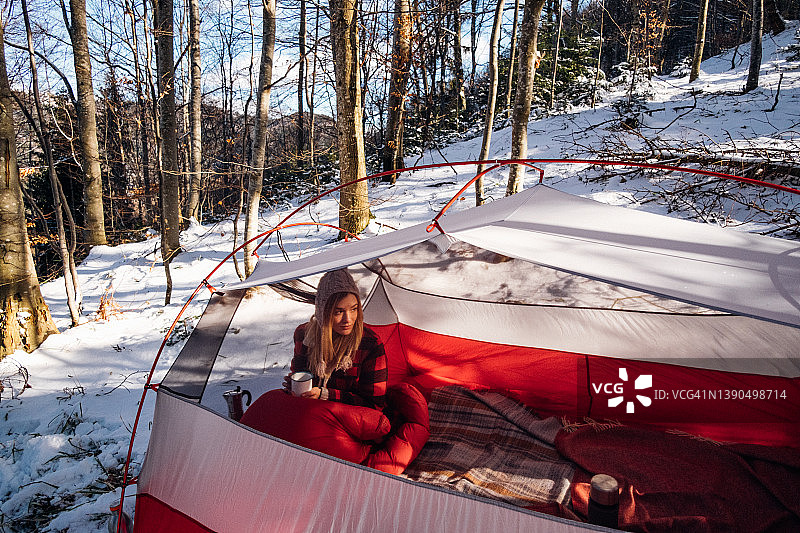女人在雪地里的睡袋里搭着红色帐篷图片素材