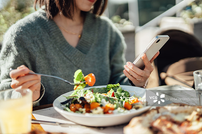 年轻女子在户外餐厅享用素食午餐时使用智能手机图片素材