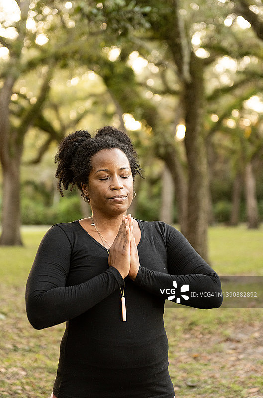 真正的非洲裔美国妇女在她40多岁的户外做瑜伽，双手在祈祷图片素材