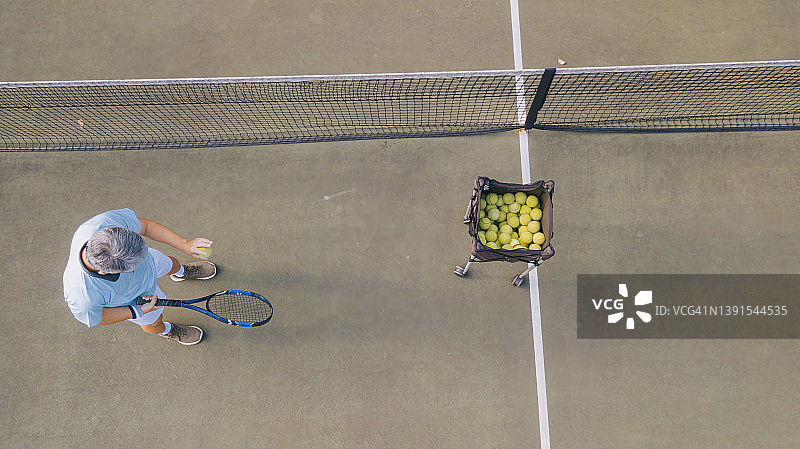 无人机视角的亚洲高级男子网球选手发球在正上方的网球场练习图片素材