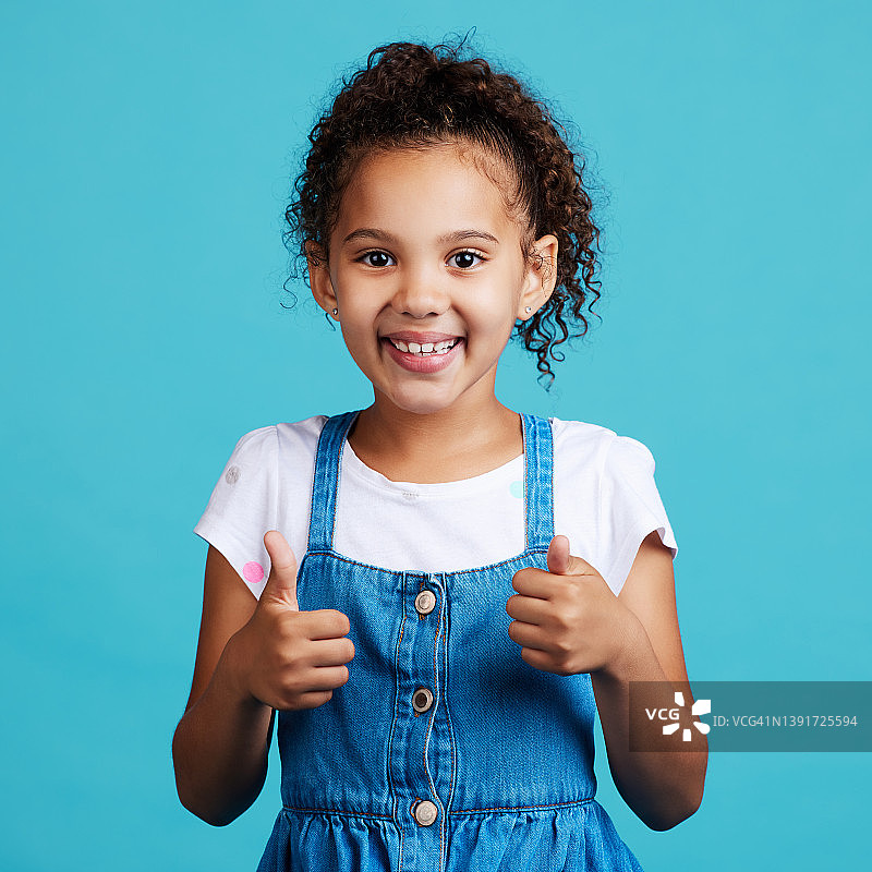 一个可爱的小女孩站在蓝色背景下竖起大拇指图片素材