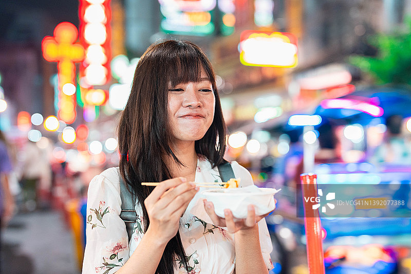 一个年轻的亚洲女人在曼谷夜市尝试一些食物图片素材