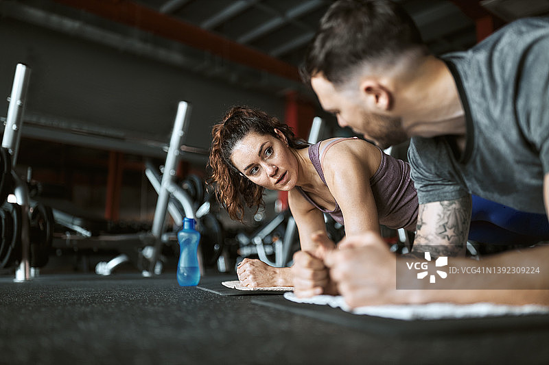 体育情侣在健身房用平板支撑的姿势交谈。图片素材