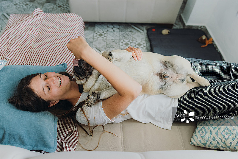 女人躺在沙发上和她的狗狗玩耍图片素材