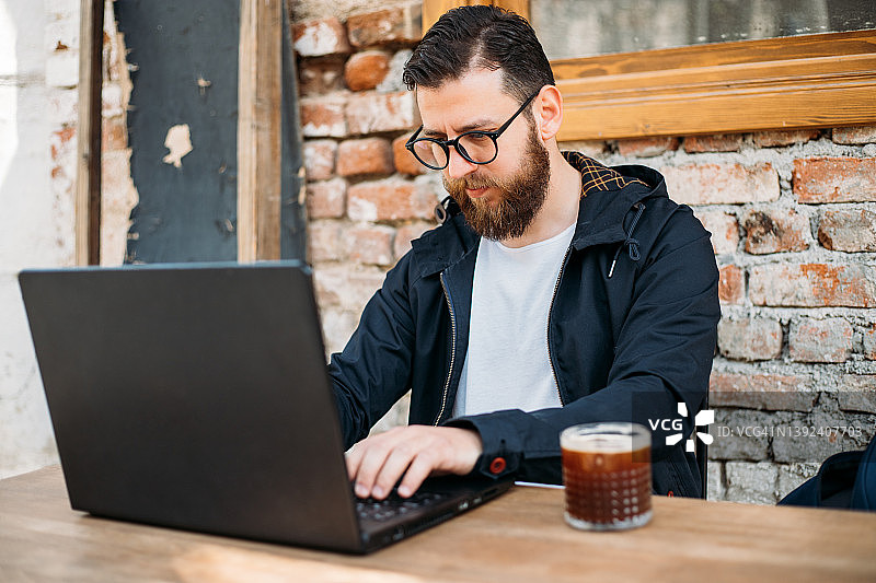 帅哥一边喝着冰美式咖啡，一边在笔记本电脑前工作图片素材