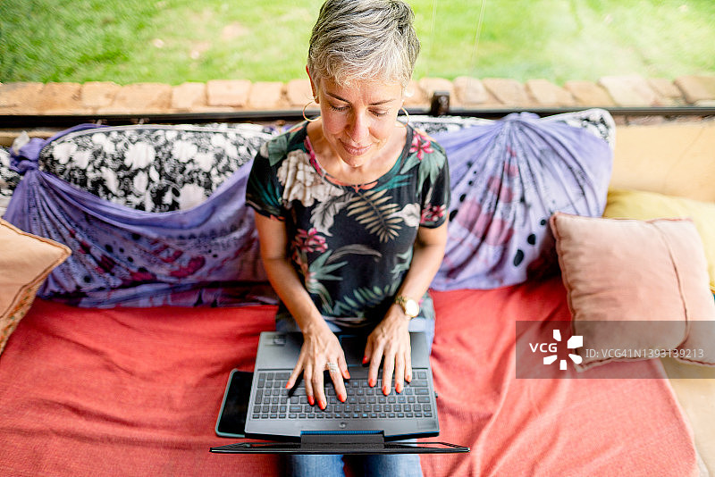 成熟的女人坐在院子里，用笔记本电脑工作图片素材