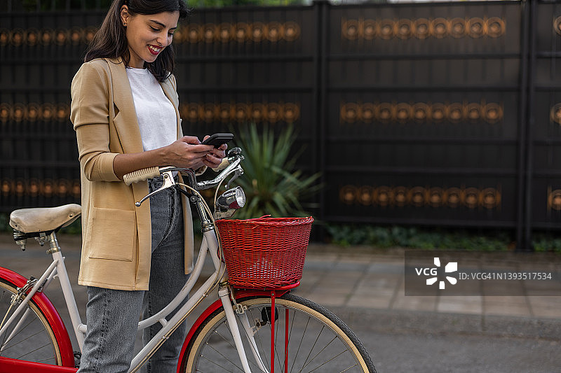 时髦的年轻女子在城市骑自行车时使用智能手机图片素材