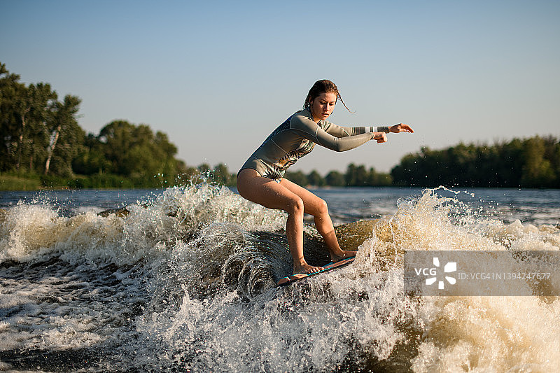 活跃灵活的女人巧妙地平衡大溅起的波浪在冲浪板上。图片素材