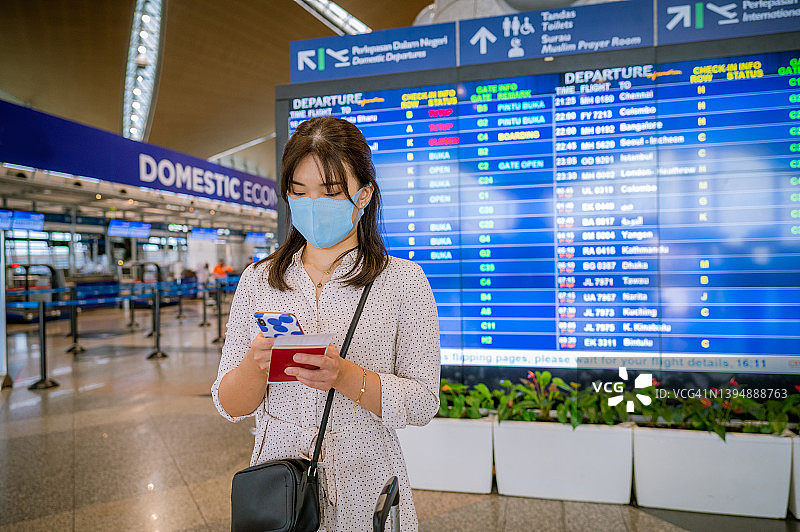 戴着口罩，在机场用智能手机查看登机日程的亚洲女性乘客a某(29岁)。在到达离港板前等候。图片素材