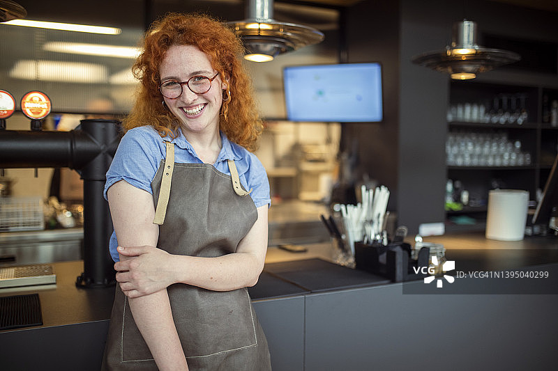 一个快乐微笑的女服务员站在咖啡店里和顾客打招呼。图片素材