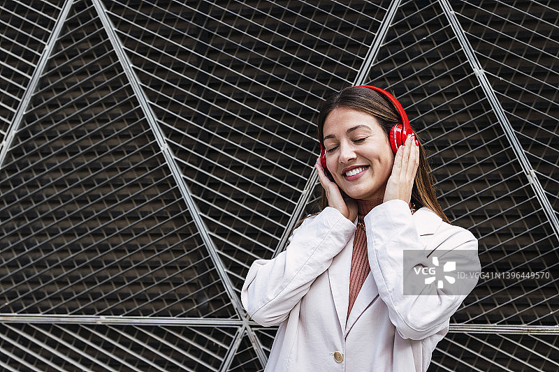 快乐的女人在金属墙前通过无线耳机听音乐图片素材
