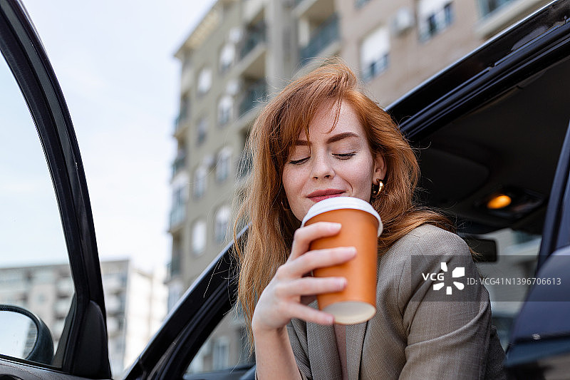 喝着咖啡的快乐年轻女子车里有刹车。一边看女人手里拿着咖啡。一个年轻女人在车里喝咖啡图片素材