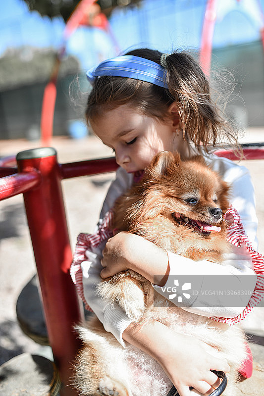 操场上可爱的女孩抱着她的博美小狗图片素材
