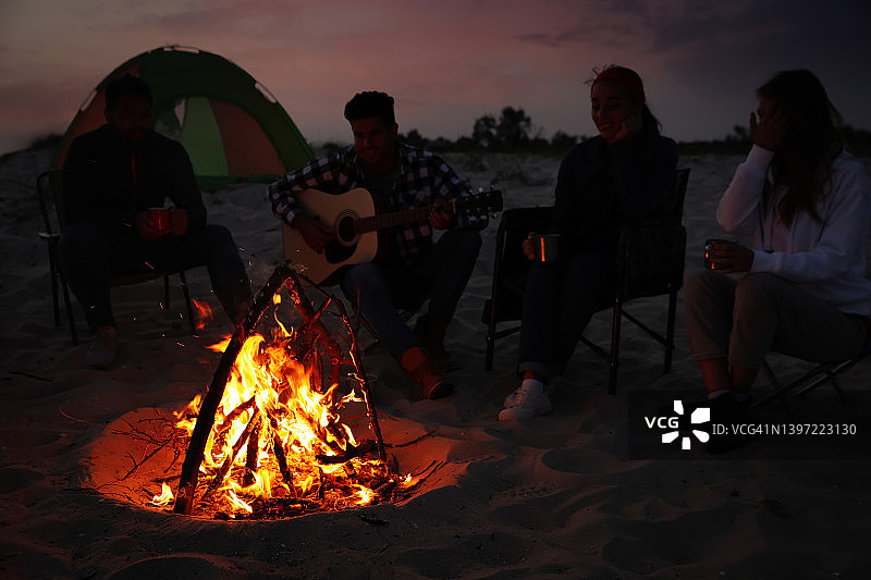 一群朋友晚上聚在海边的篝火旁。露营的季节图片素材