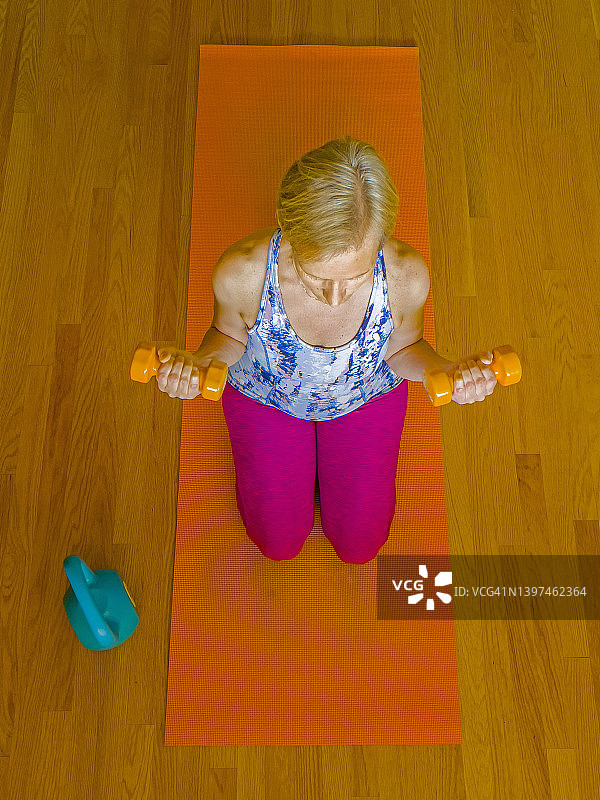 一个女人坐在橙色垫子上做瑜伽姿势和举重运动的俯瞰视图图片素材
