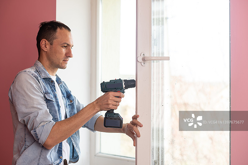 勤杂工使用无绳螺丝刀安装窗户把手。合格工人服务，家居维修和装修。图片素材