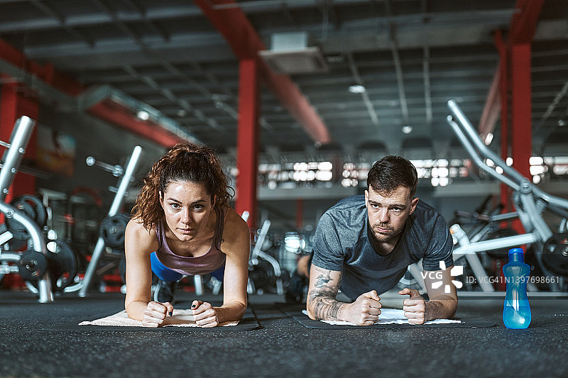 一对运动员夫妇在体育馆做平板支撑练习耐力。图片素材
