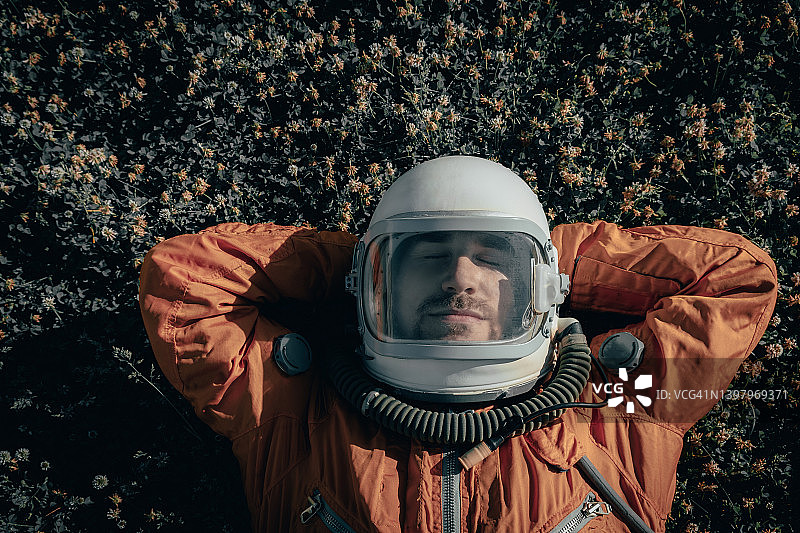 宇航员穿着太空服，戴着太空头盔，躺在户外草地上打盹的特写。宇航员在草地上睡觉的肖像图片素材