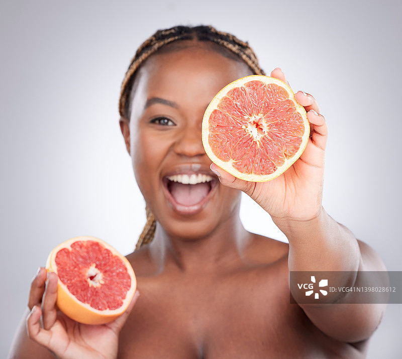 工作室拍摄了一个迷人的年轻女子拿着一个切片葡萄柚对灰色的背景图片素材