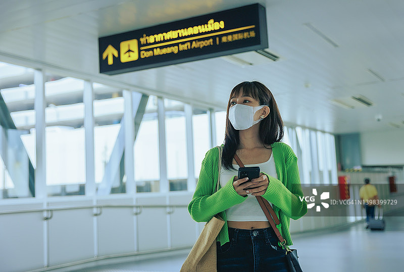 年轻的亚洲女商人戴着口罩，在机场用手机阅读电子邮件。商务旅行的概念。图片素材