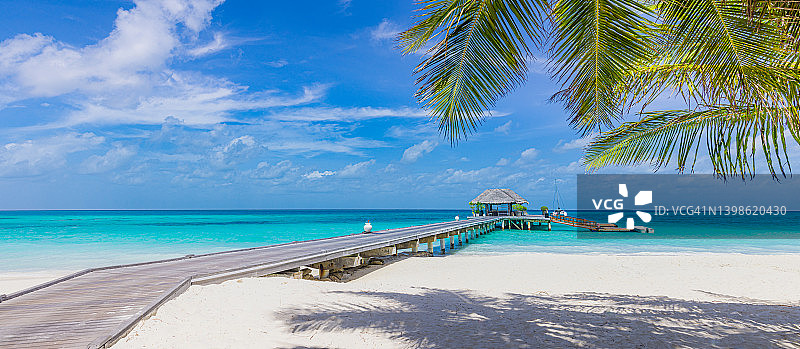 豪华酒店的水上别墅和棕榈树叶子在白色的沙滩，接近蓝色的大海，海景。沙滩椅，带白色雨伞的床。暑假和假期，在热带海岛度假海滩图片素材