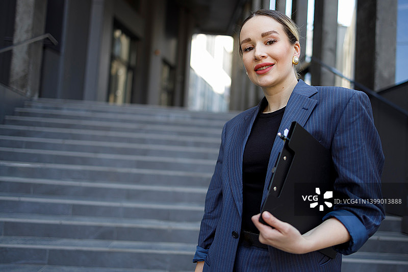 有魅力的商业女性手里拿着一个夹纸夹站在现代建筑的楼梯上图片素材