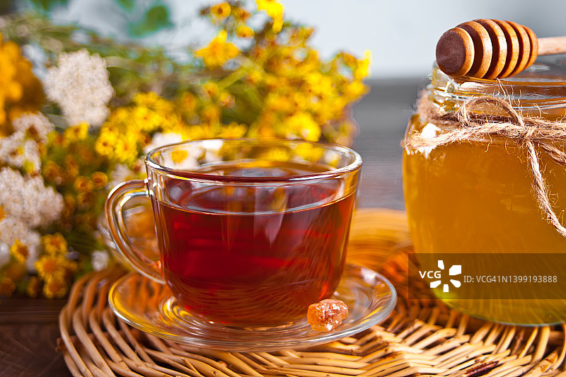 一杯花草茶，鲜花，蜂蜜在罐子里，茶壶和各种干燥的草药在托盘上。图片素材