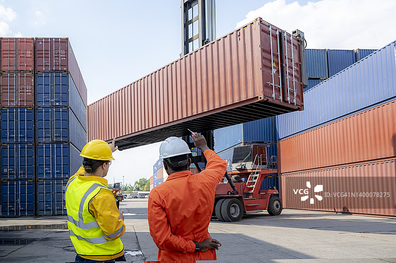 两名工人对货物集装箱进行讨论，控制从货物运输船上装载集装箱图片素材